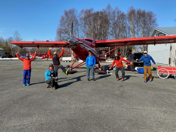 Six socially distanced unmasked climbers outside a small aircraft