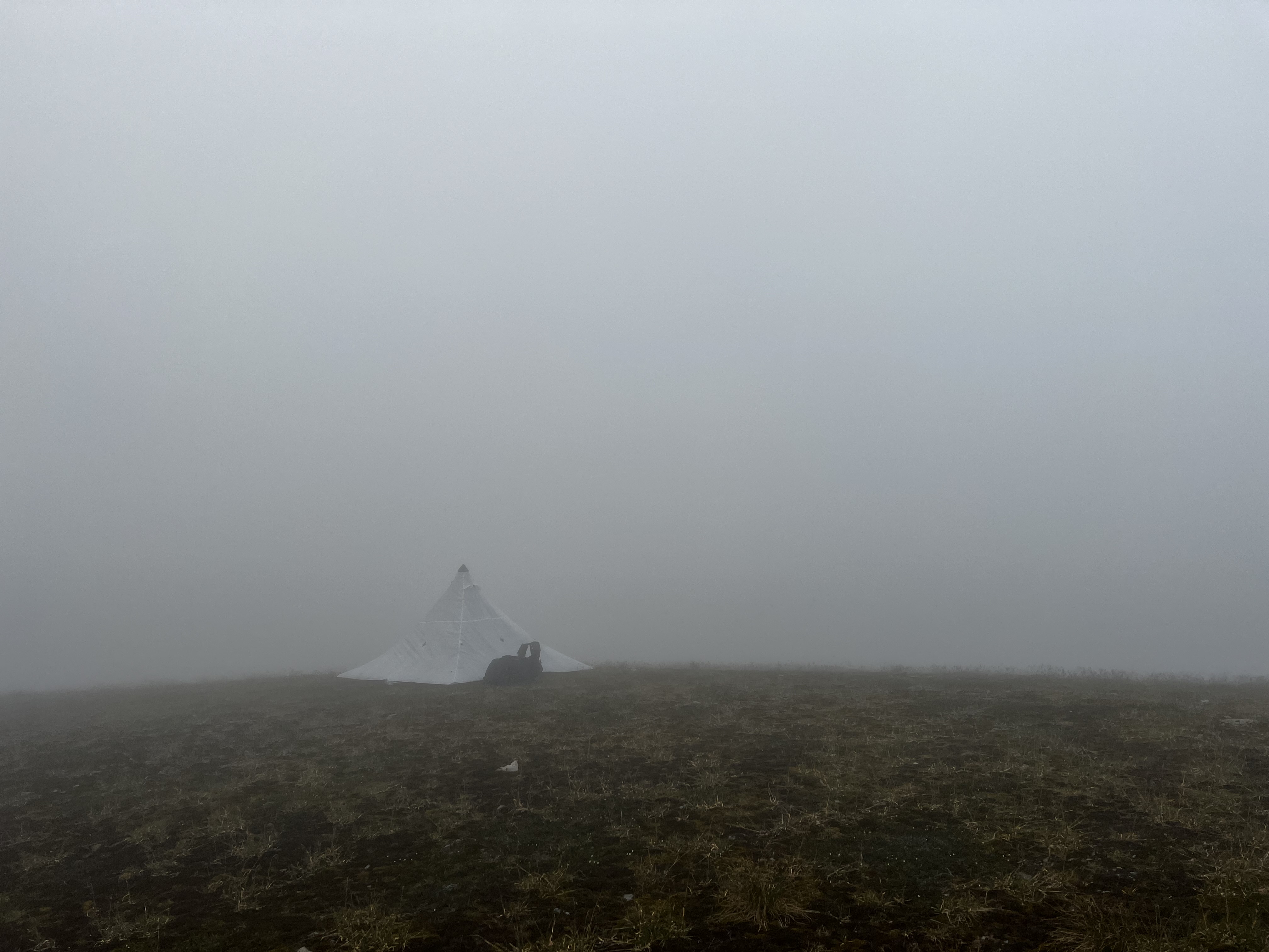 The silhouette of tent pitched on tundra against a backdrop of dense fog