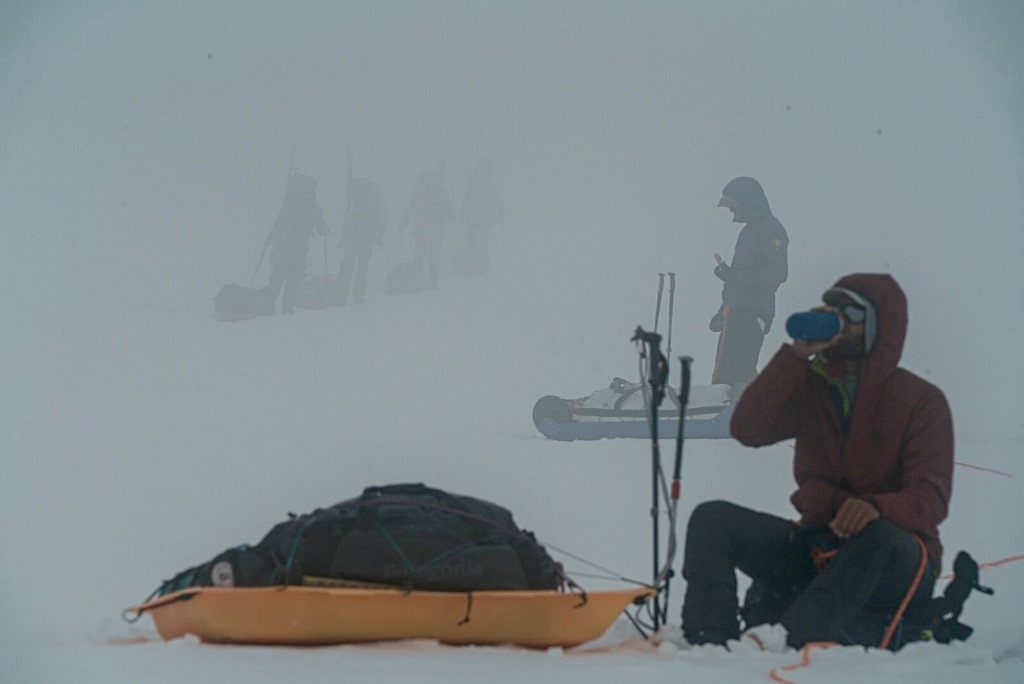 Water break On a foggy glacier, a climber sits next to his sled and enjoys a bottle of water