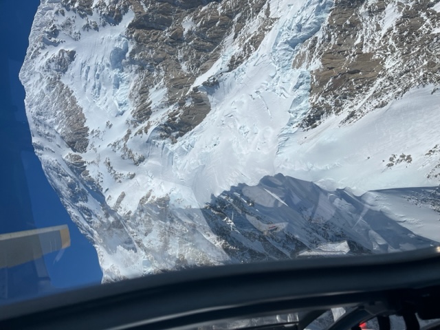 West Rib, taken the week of April 22, 2024 Image looking out the window of a helicopter down at a snow and ice covered mountain ridge