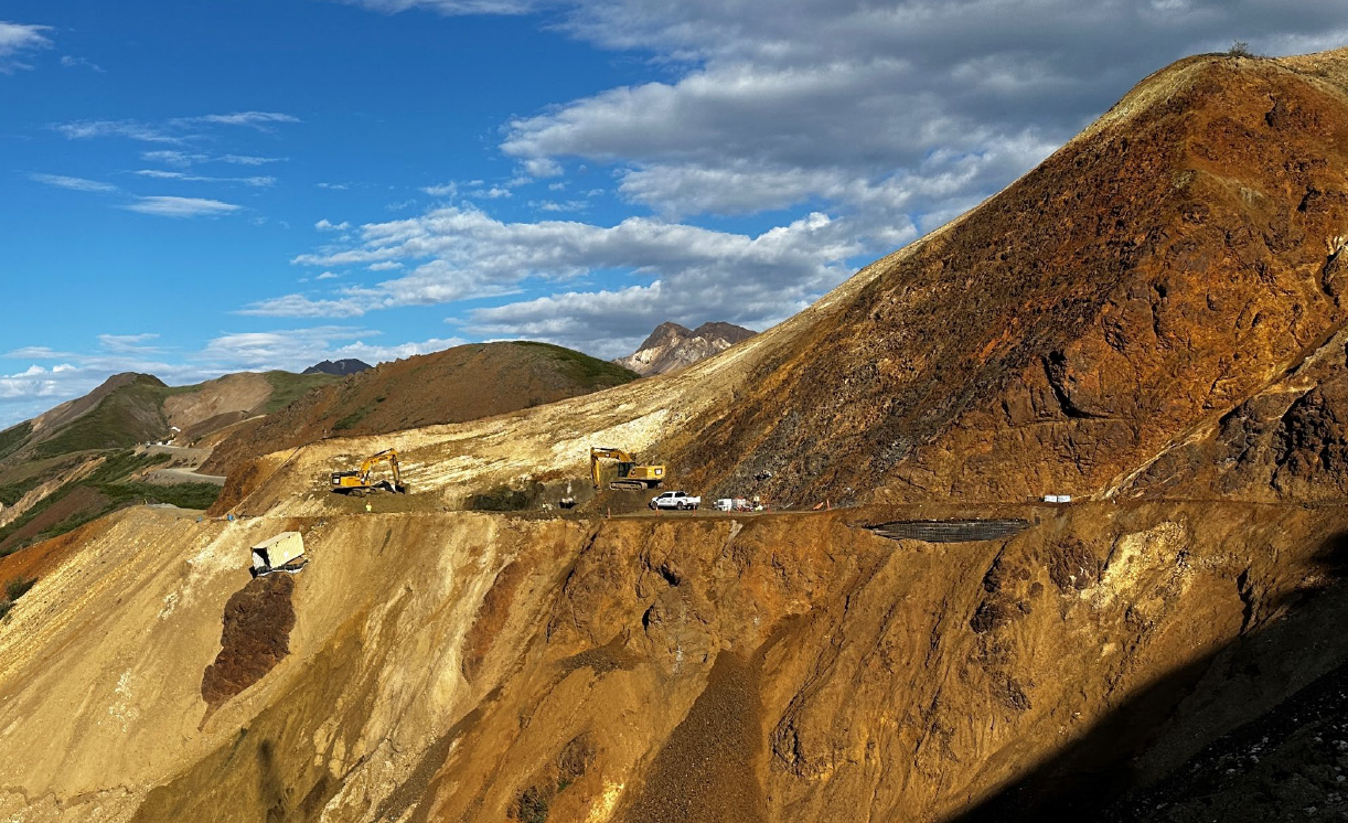 West Cut Excavation Nearing Completion Construction equipment digs along a steep cliff of colorful rocks with a road cut through it.