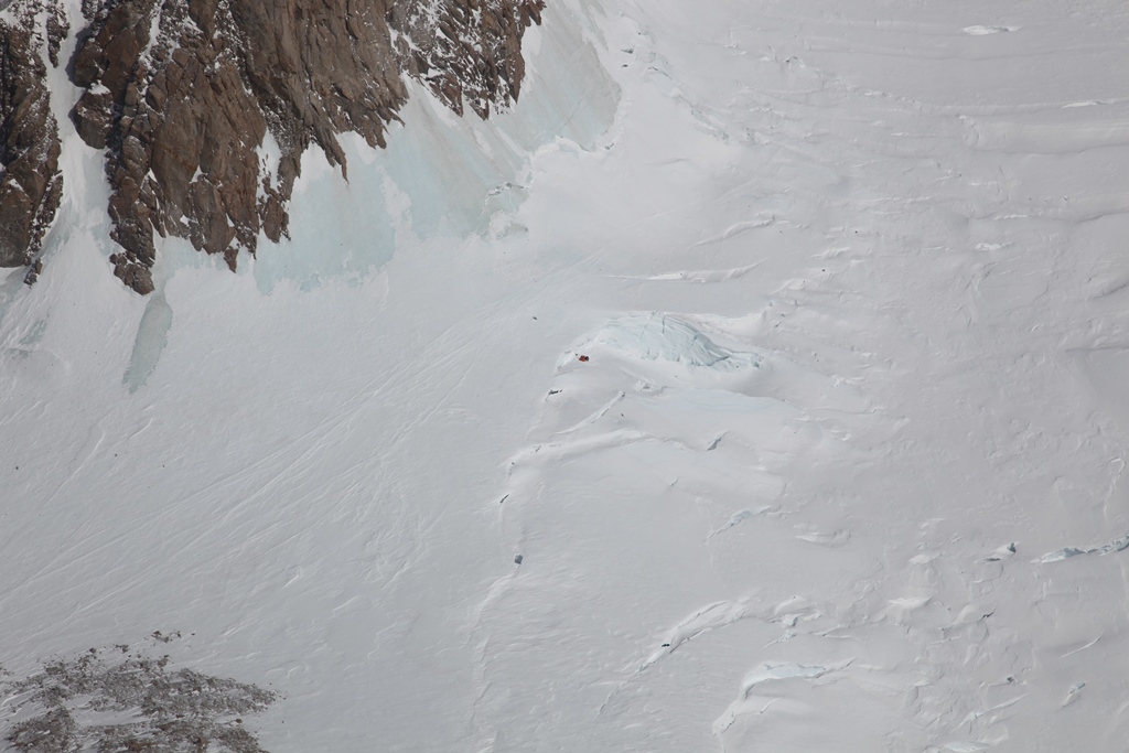 Helicopter view of a crevassed glacier below with a small tent visible