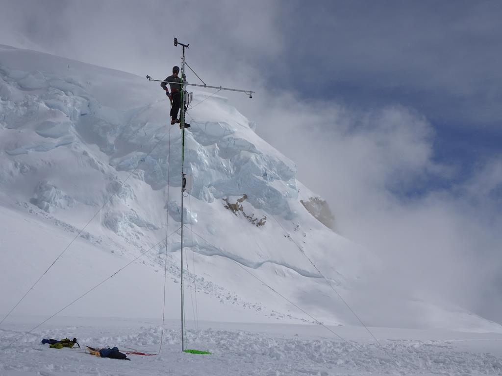 Weather Station testing at 14,200 feet A park ranger climbs a tall metal pole to install weather equipment