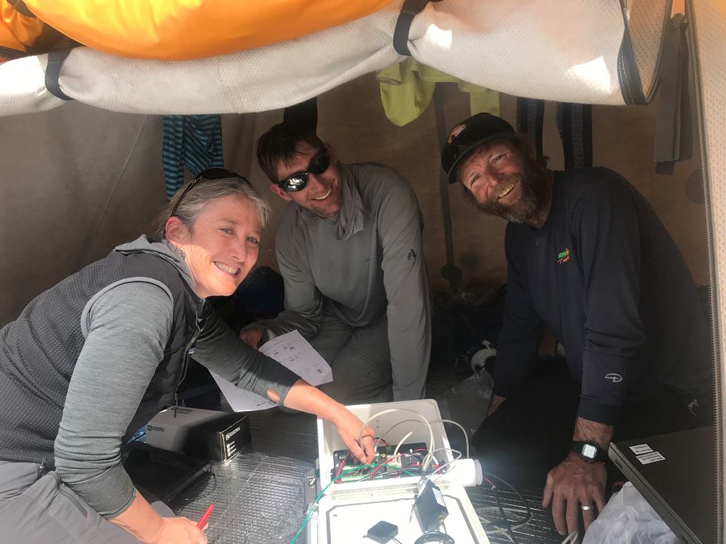 The weather stations are multi-disciplinary collaboration Three scientists troubleshoot the weather station equipment in a tent at Basecamp