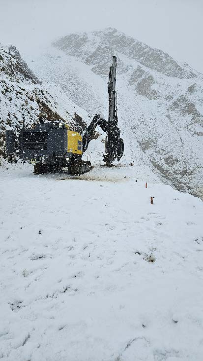 An inch of snow covers the road and snow continues to fall as heavy machinery drills down into the roadbed rock on the west side of Pretty Rocks.