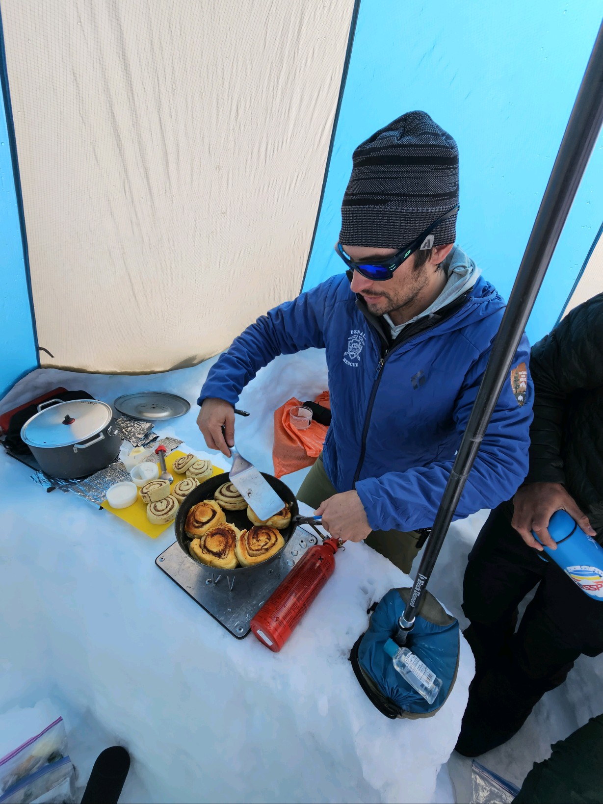 A man in a cooktent prepares cinnamon rolls in a cast iron skillet