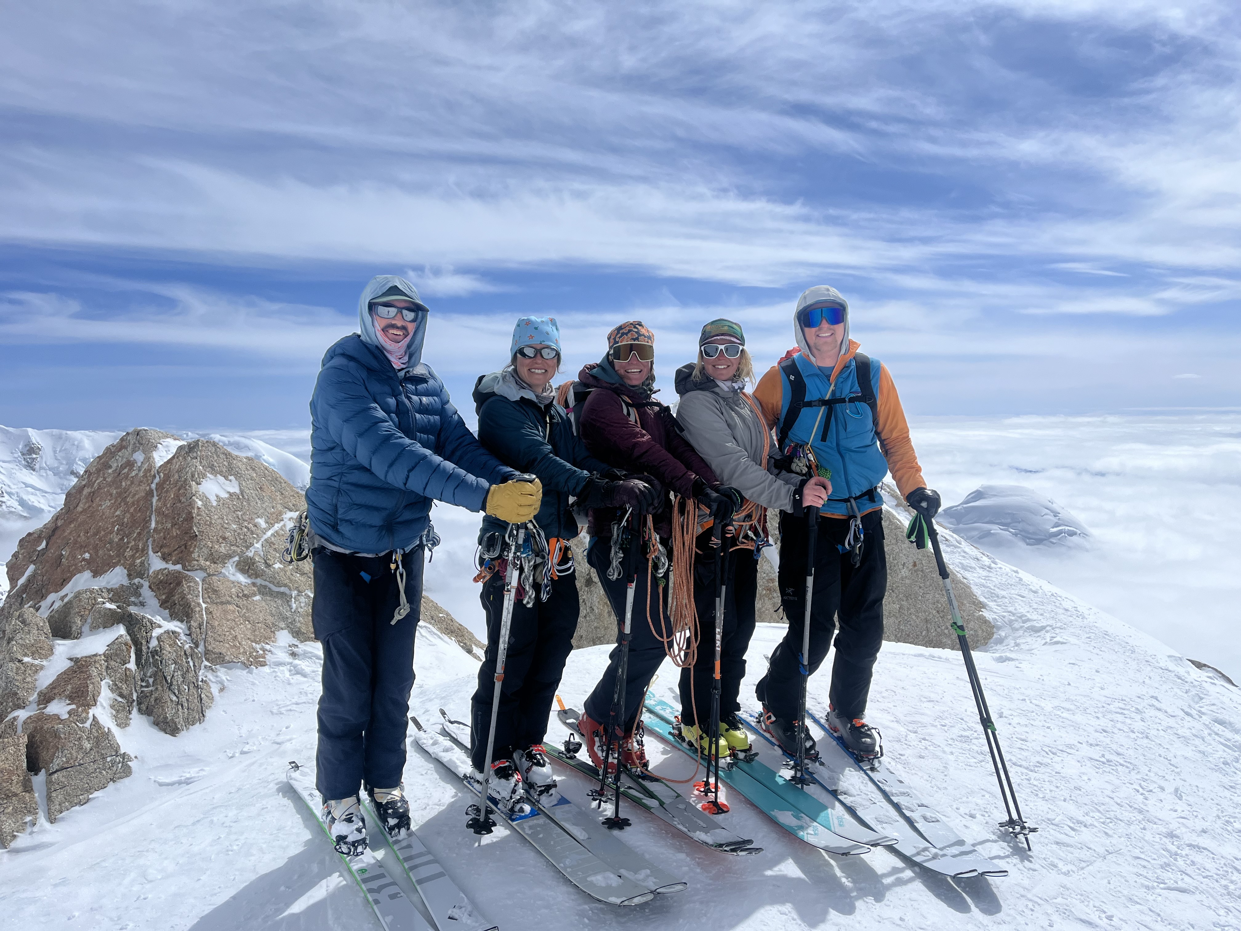 A line up of five skiers pose on a mountain ridge