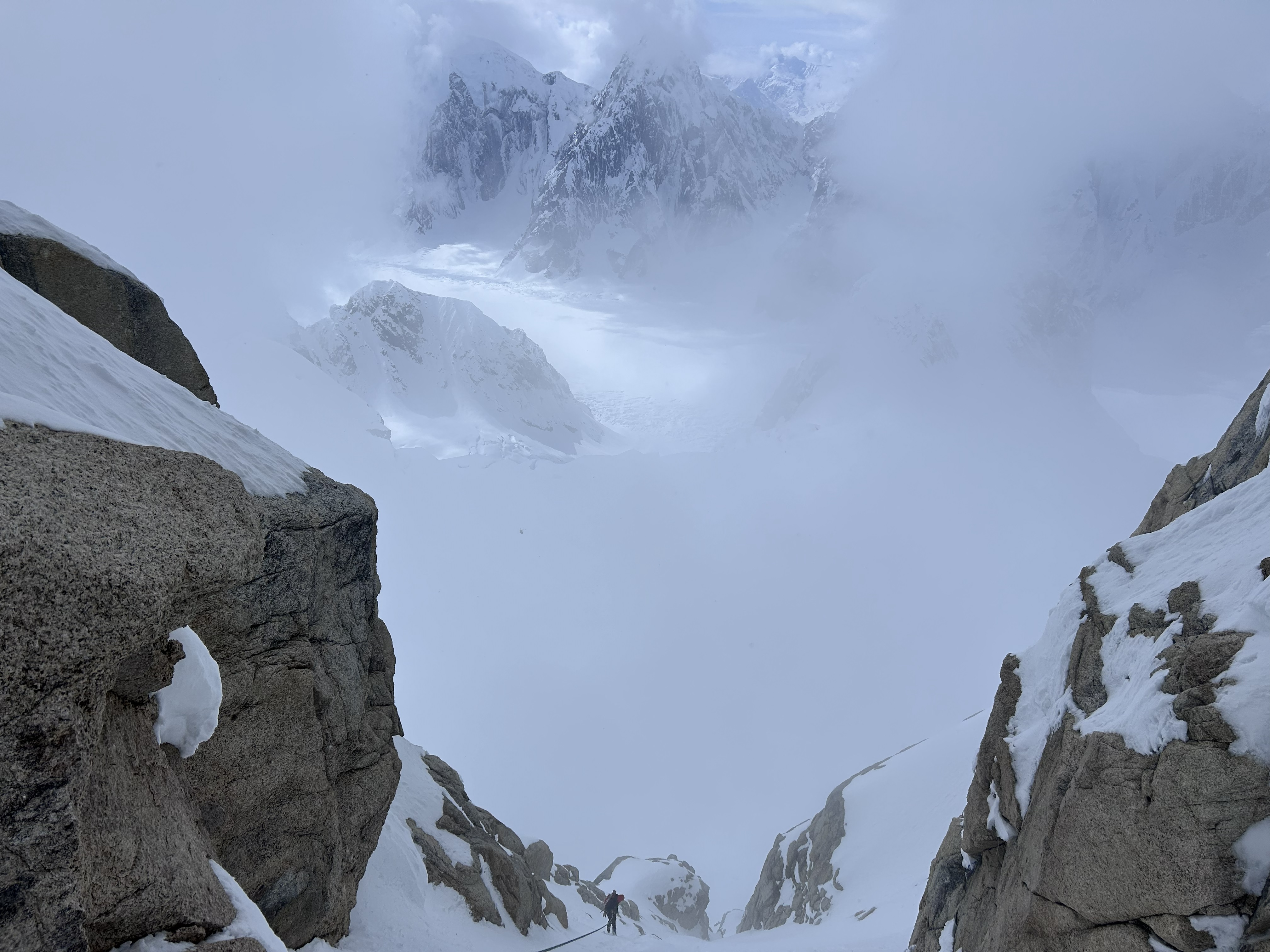 rappels off of fixed anchors a ranger far in the foreground using fixed anchors to rappel through a snow-covered pitch towards a foggy section