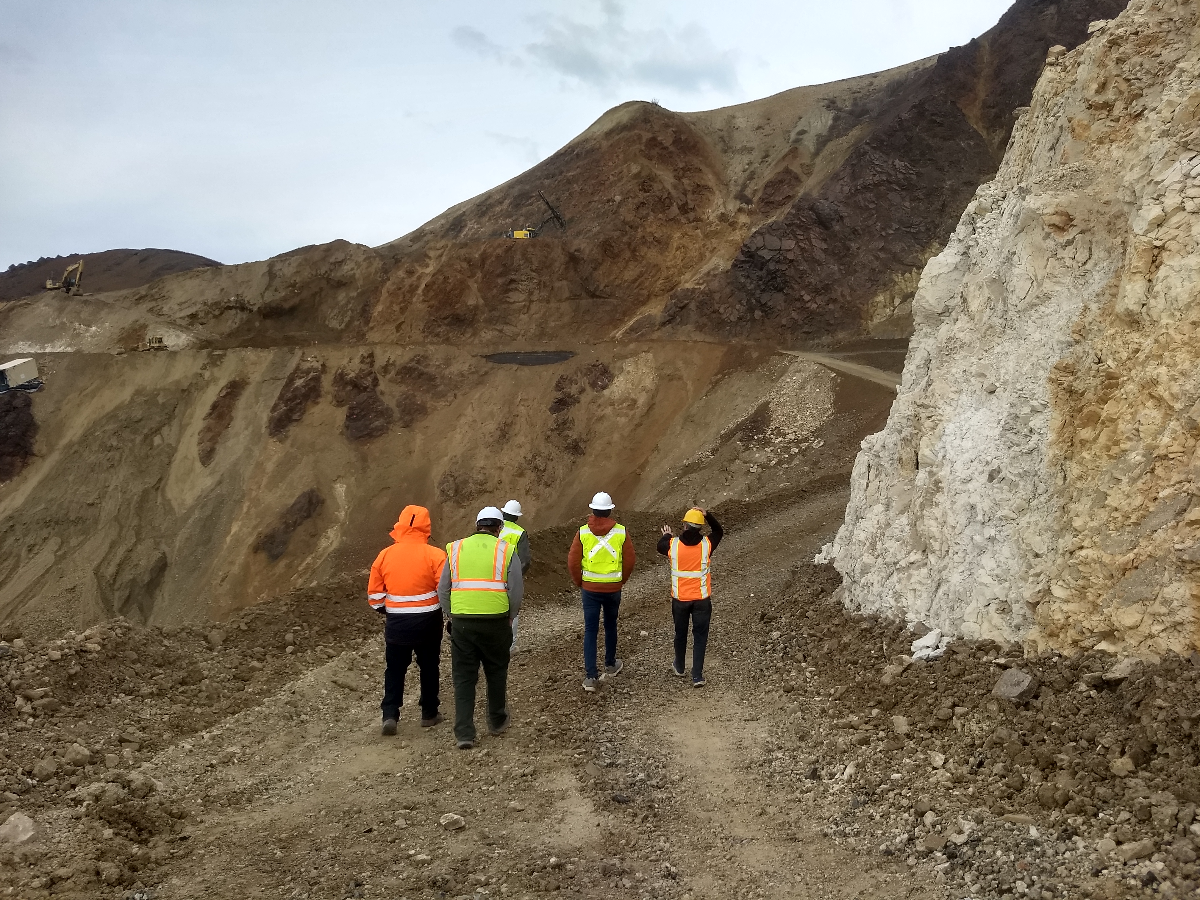 site visit May 2024 Five people in safety vests and hard hats walk toward the west side of the landslide where several pieces of construction equipment can be seen working.