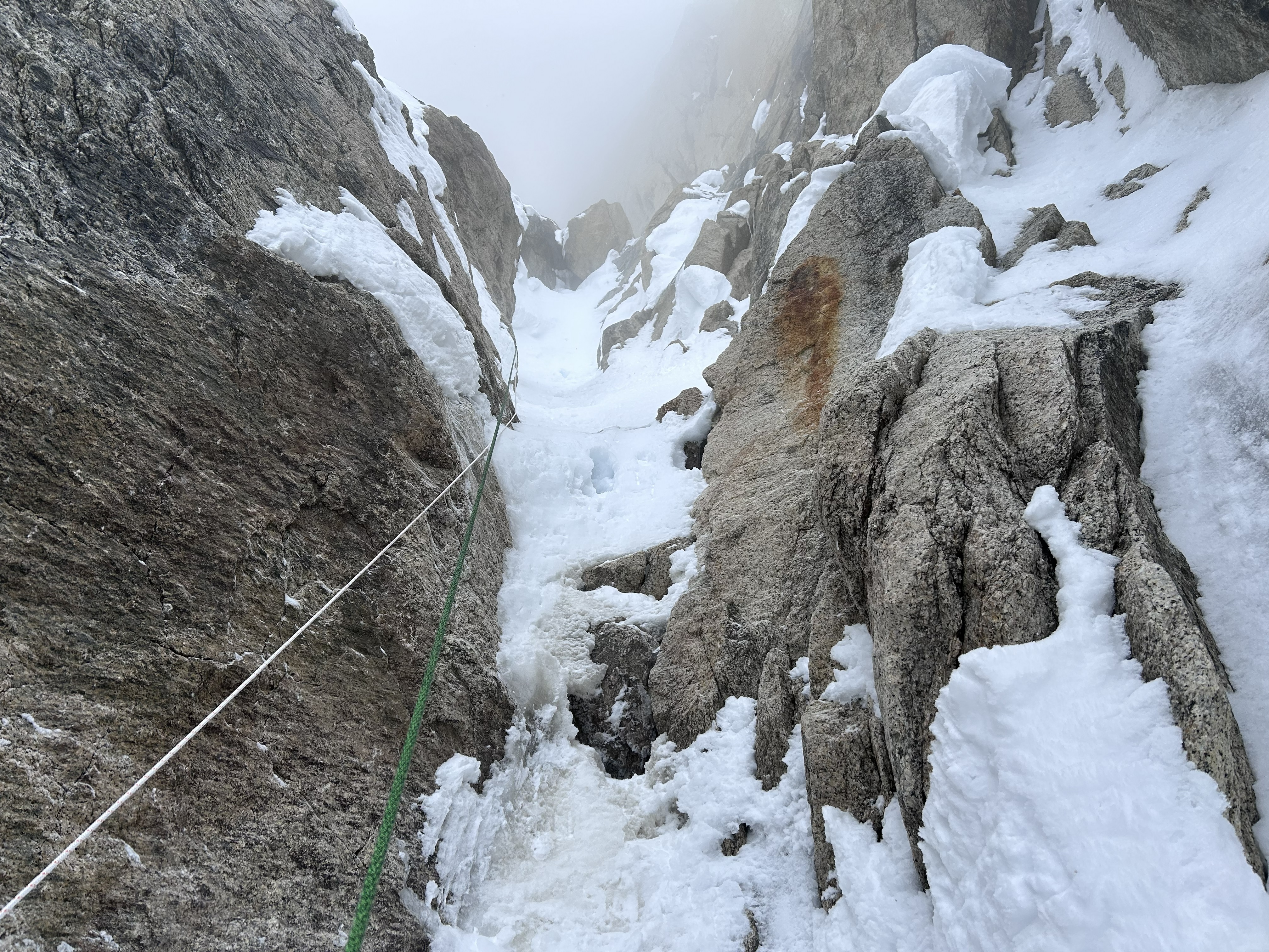 start to the 5.9 rock pitch A white rope and green rope hanging down a snowy rock pitch