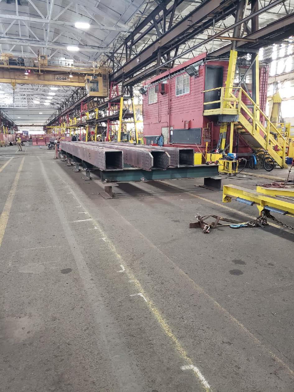 steel fabrication 2 FHWA Three large metal beams in a warehouse surrounded by construction equipment.