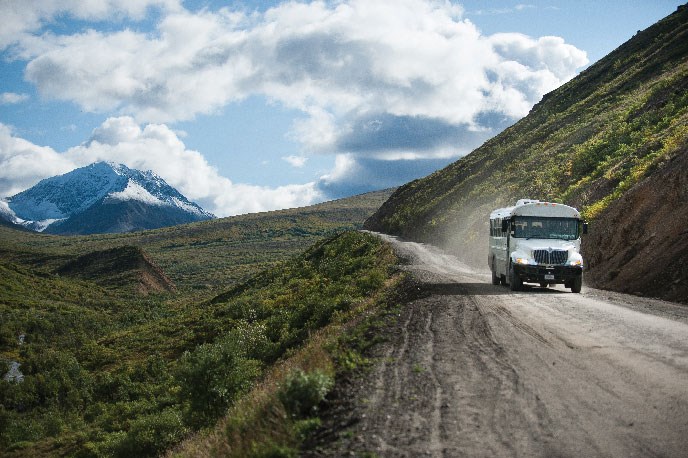 A white bus travels along a gravel road