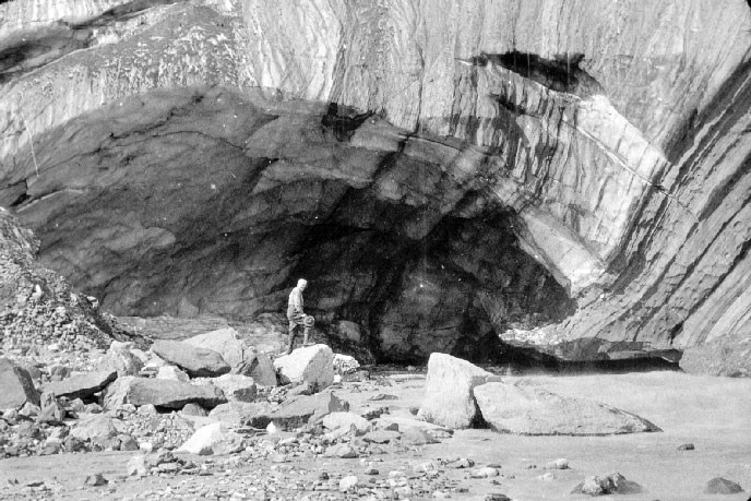 Historic image of a park ranger standing at the opening of a glacier