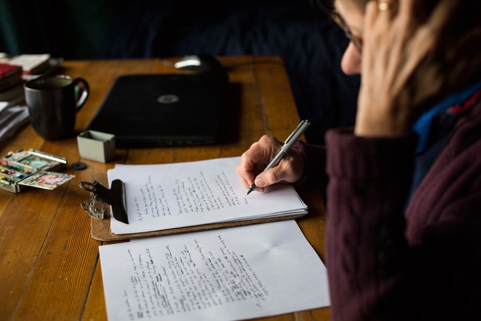 Woman conentrating at a wood table writes with a pen on white unlined paper on a clipboard Woman conentrating at a wood table writes with a pen on white unlined paper on a clipboard