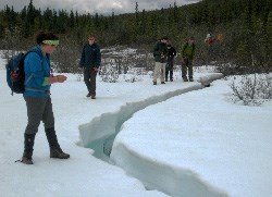 Young people peer into an opening across a field of snow and ice