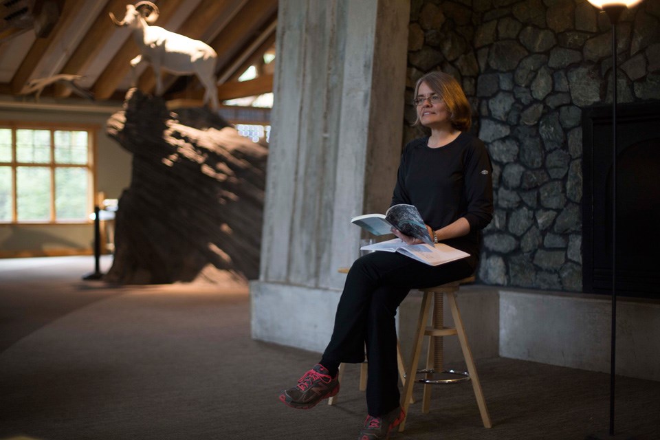 Woman on a wooden stool reads aloud from a book in an open exhibit space Woman on a wooden stool reads aloud from a book in an open exhibit space