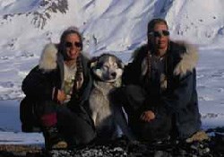 Two women wearing parkas pet a husky sled dog