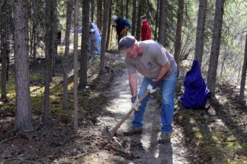 man in foreground working on trail digging up a tree root