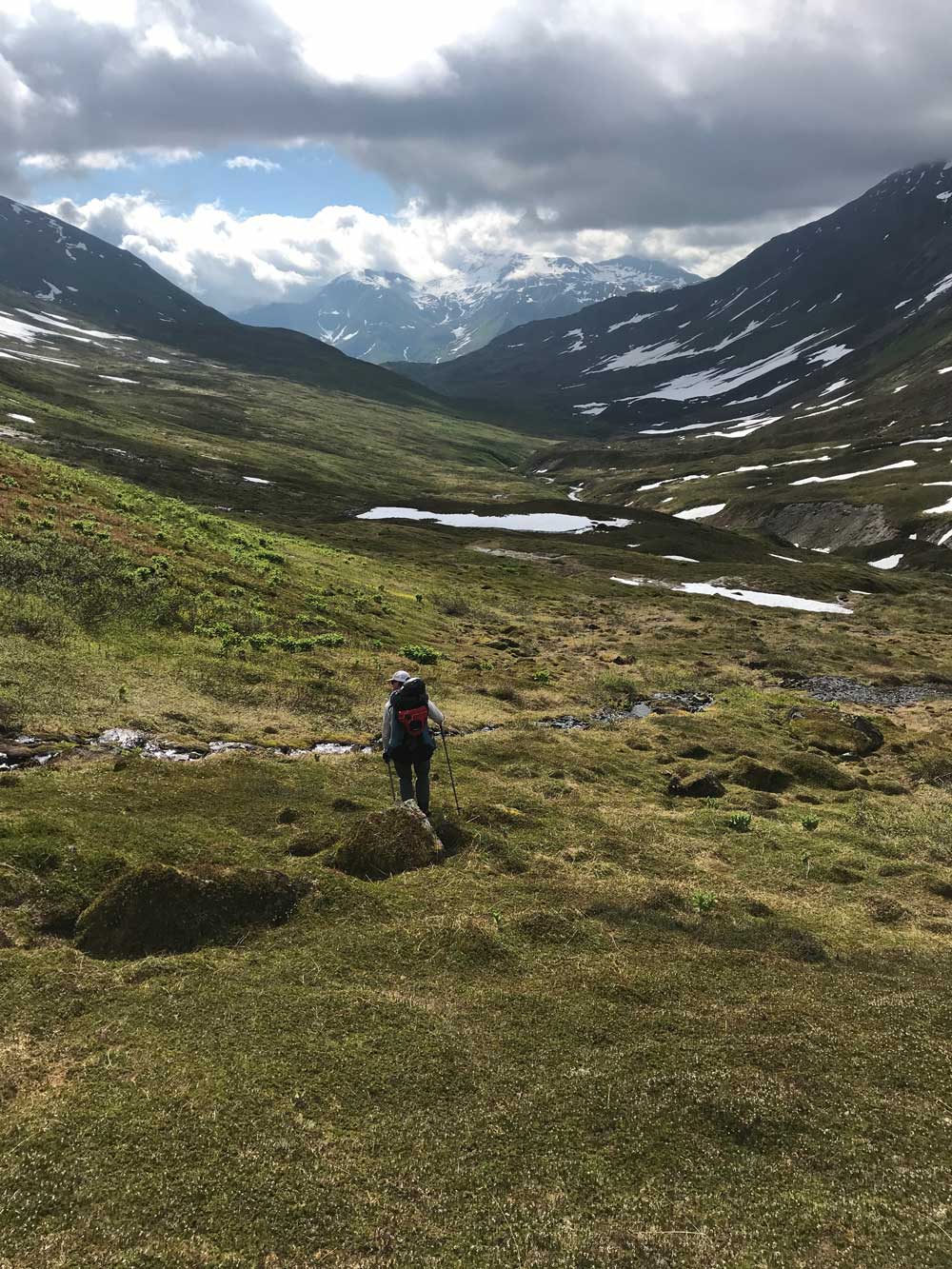 5 man walking down a narrow valley devoid of trees, between tall mountains