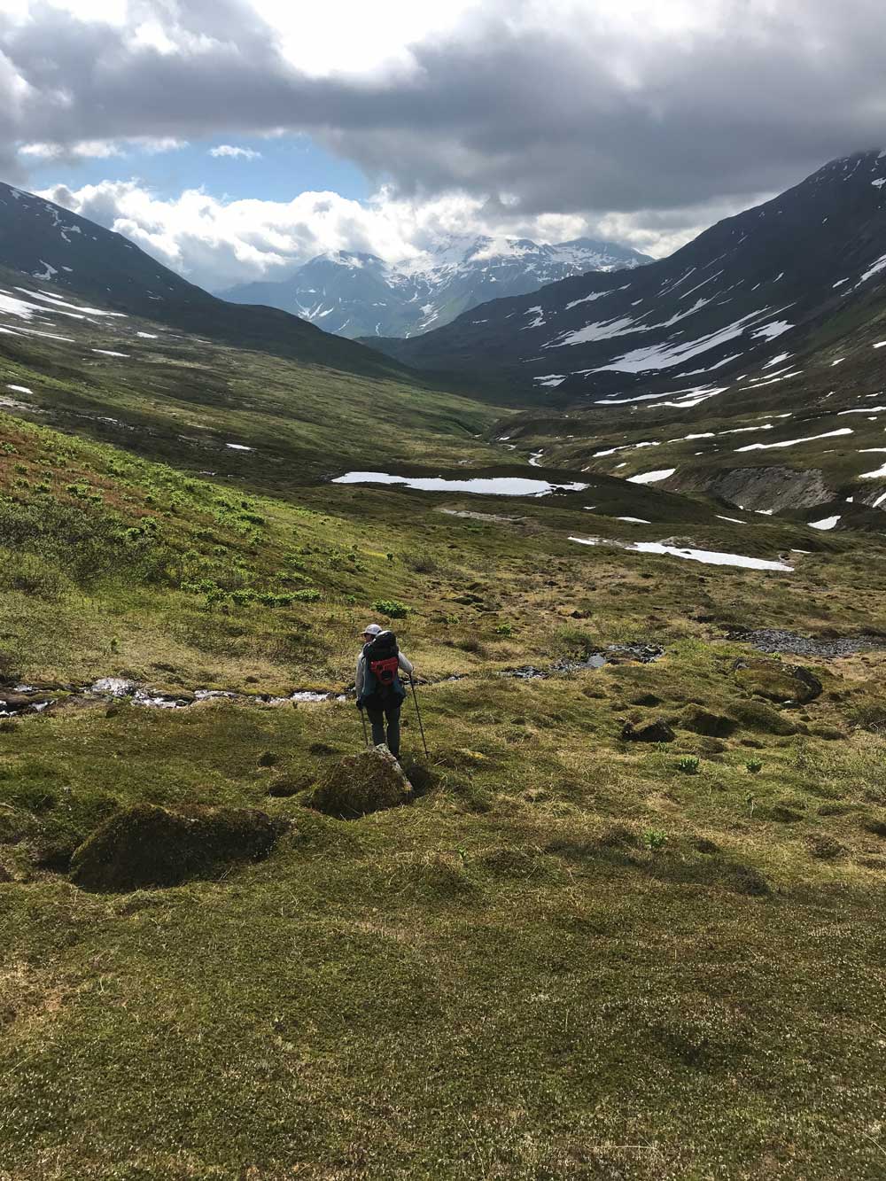 man walking down a narrow valley devoid of trees, between tall mountains