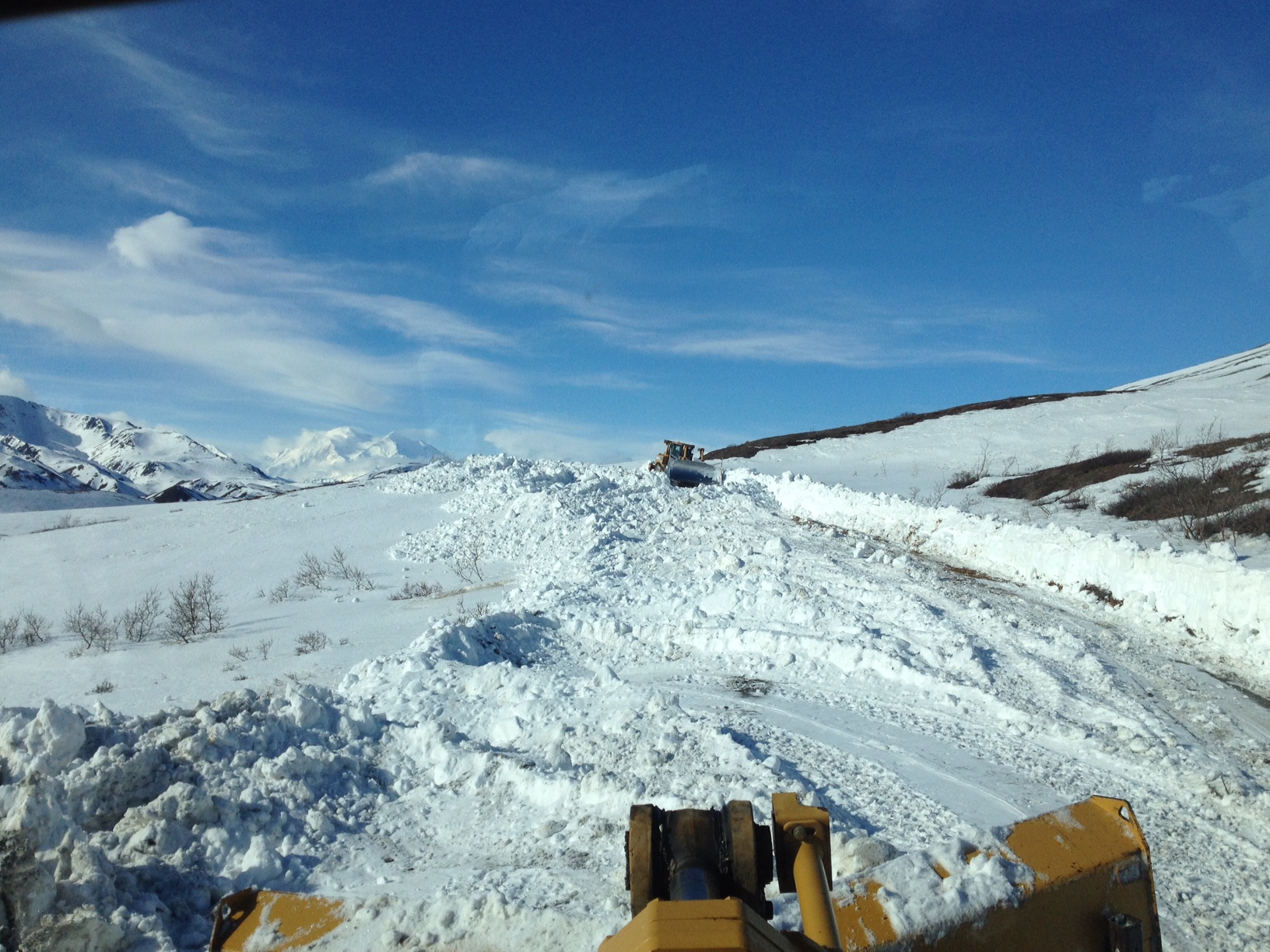 two large machines plow a snowy road on a hillside under a beautiful blue sky two large machines plow a snowy road on a hillside under a beautiful blue sky