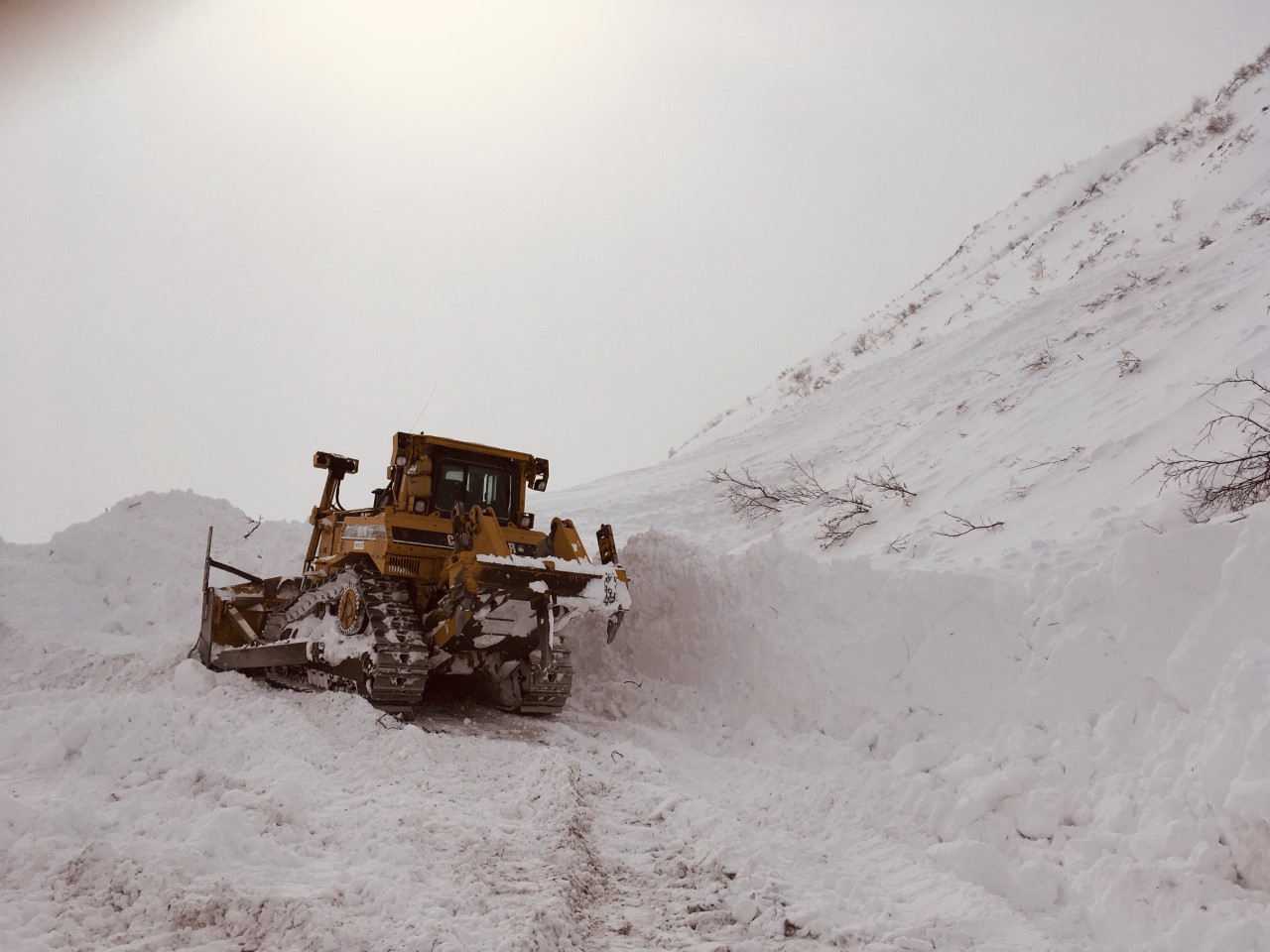 snowy mountain landscape with machinery working to plow a road
