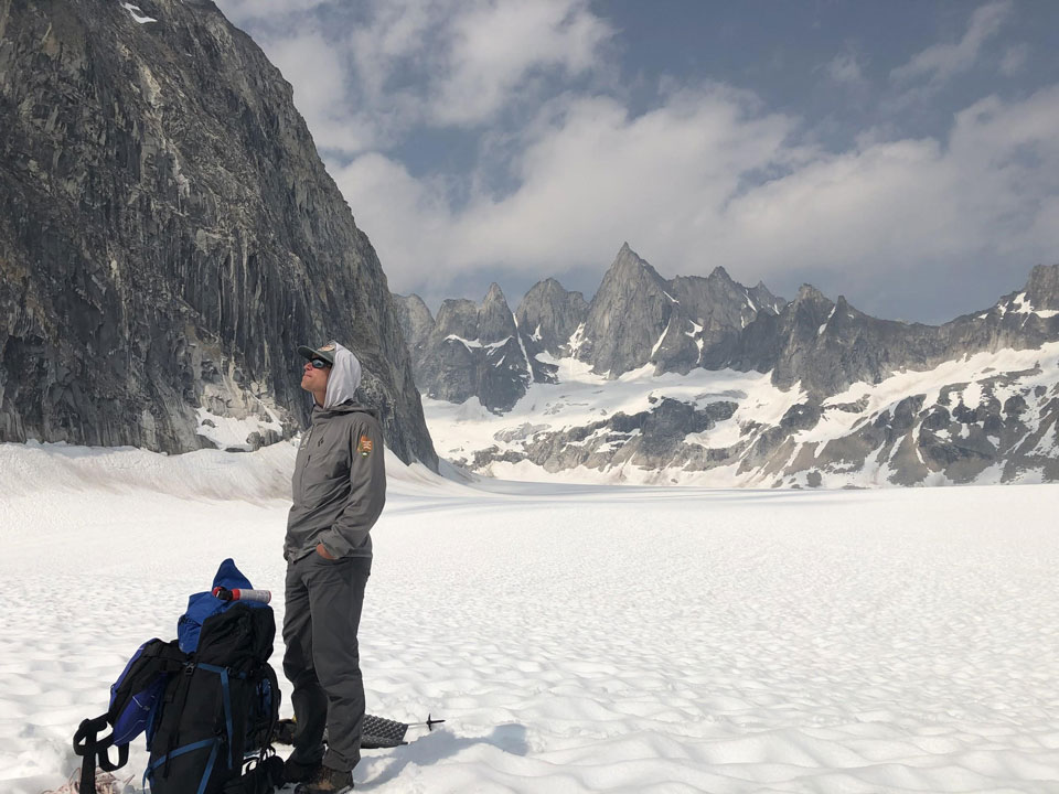 kichatna-1 a man standing on a glacier near a steep mountain