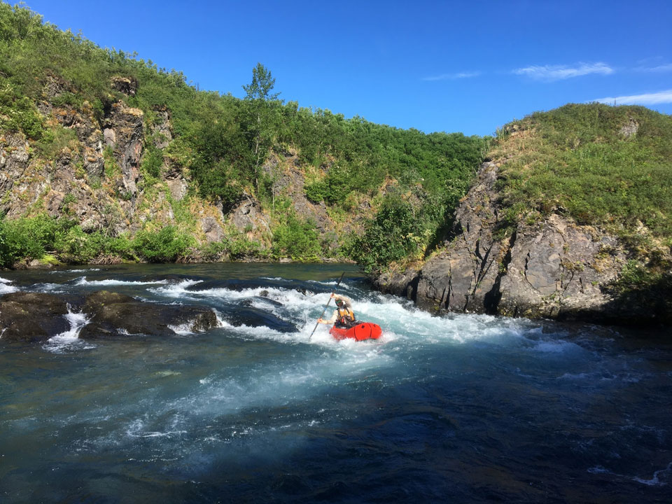 kichatna-6 man floating in a raft through a small rapid on a creek