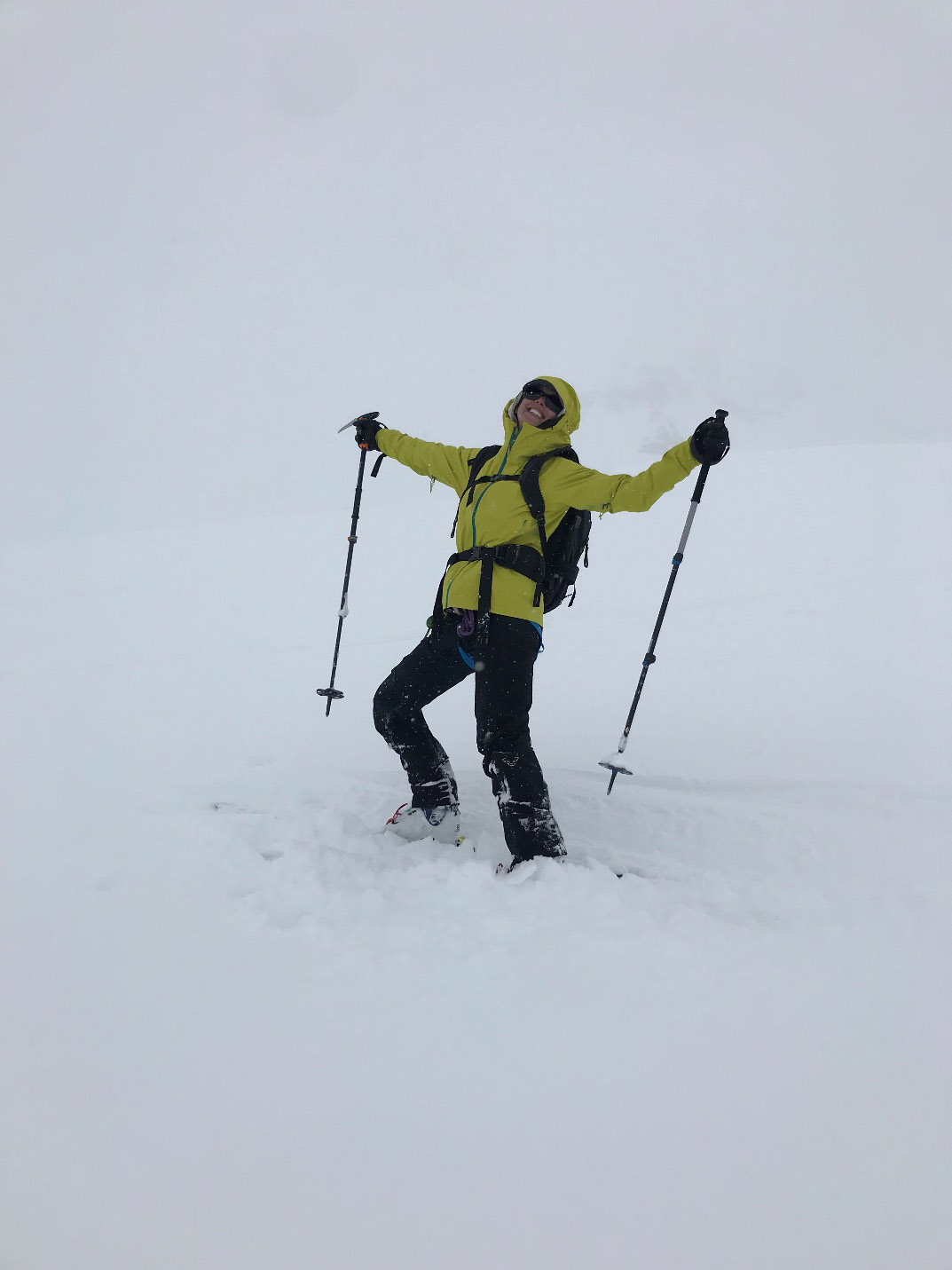 female mountaineer posing with arms raised celebratorily on a steep snowy slope