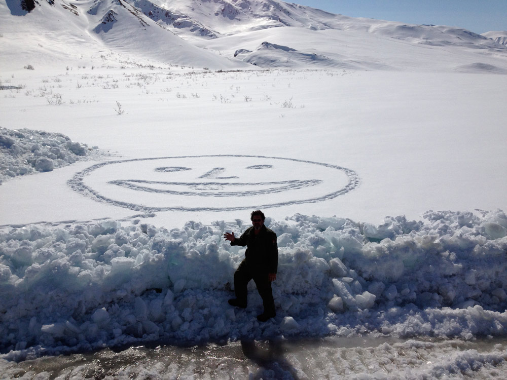 man standing near a snowy field in which a smiley face has been stomped in the snow man standing near a snowy field in which a smiley face has been stomped in the snow