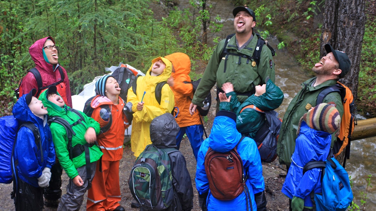 a group of young visitors and two park rangers stand in a circle tasting rain and laughing