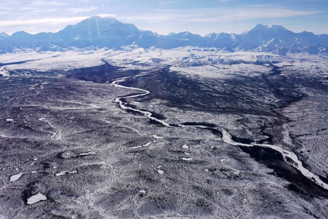 Snowy mountains of the Alaska Range tower over loawlands dotted with rivers and lakes below