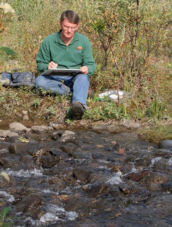 Artist Kesler Woodward sketches alongside a creek.