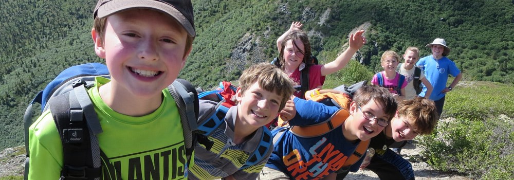 a group of campers smile and wave while hiking up a mountainside