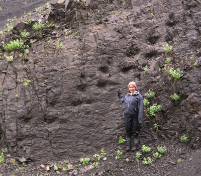 a girl stands next to a dinosaur trackway