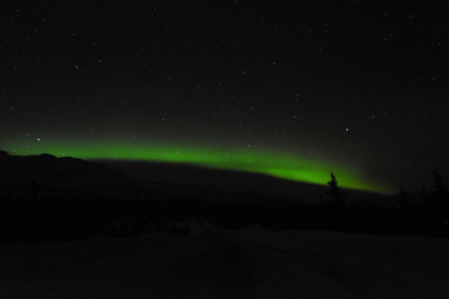 A single band of green aurora across a dark sky.