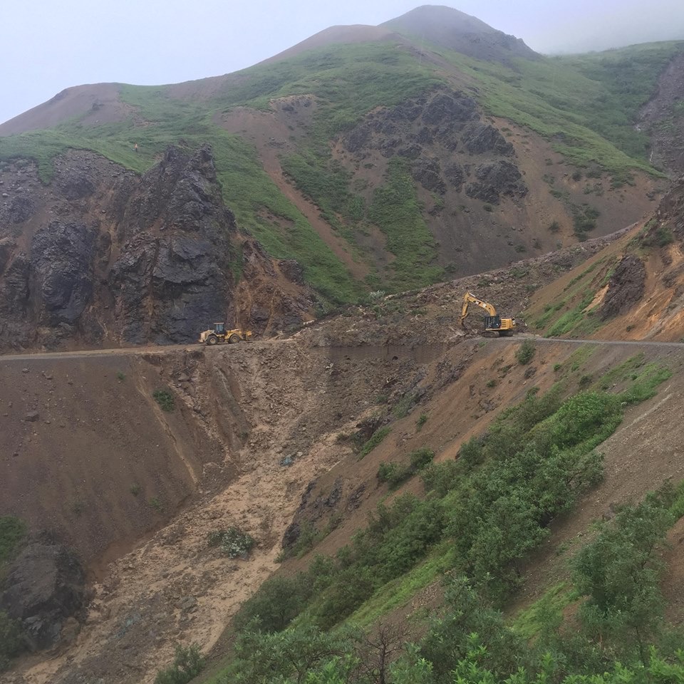 road equipment pushing a huge mud and rock slide off of a road on the side of a mountain