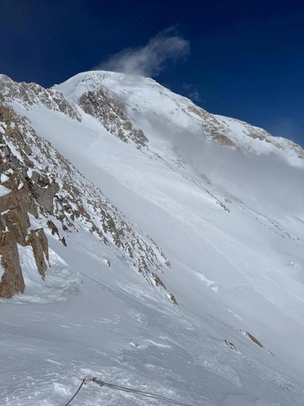 A snowy mountain gully with fixed lines at the bottom and a bright blue sky.
