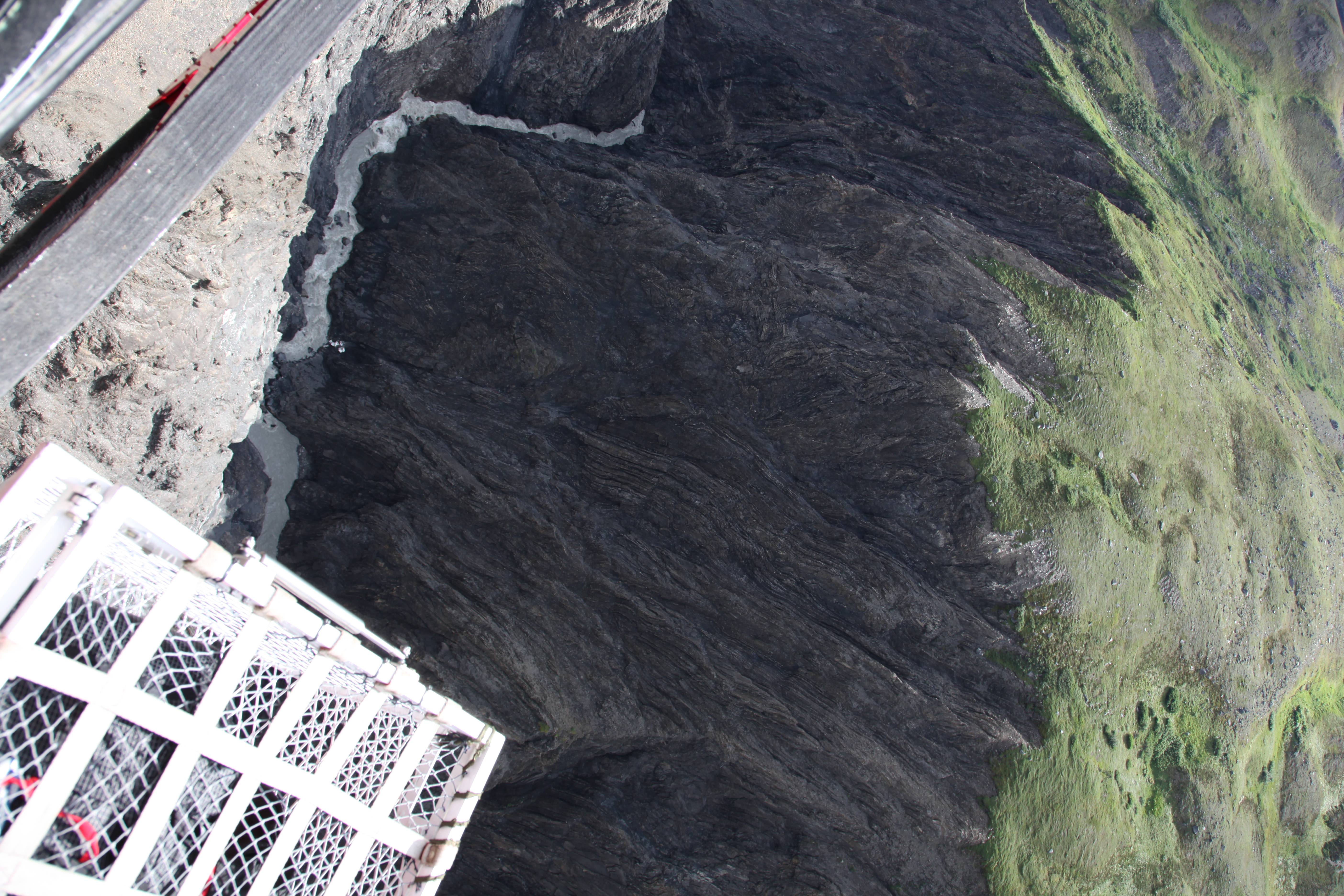 View looking down into a steep canyon with a small white pile of debris next to a flowing creek