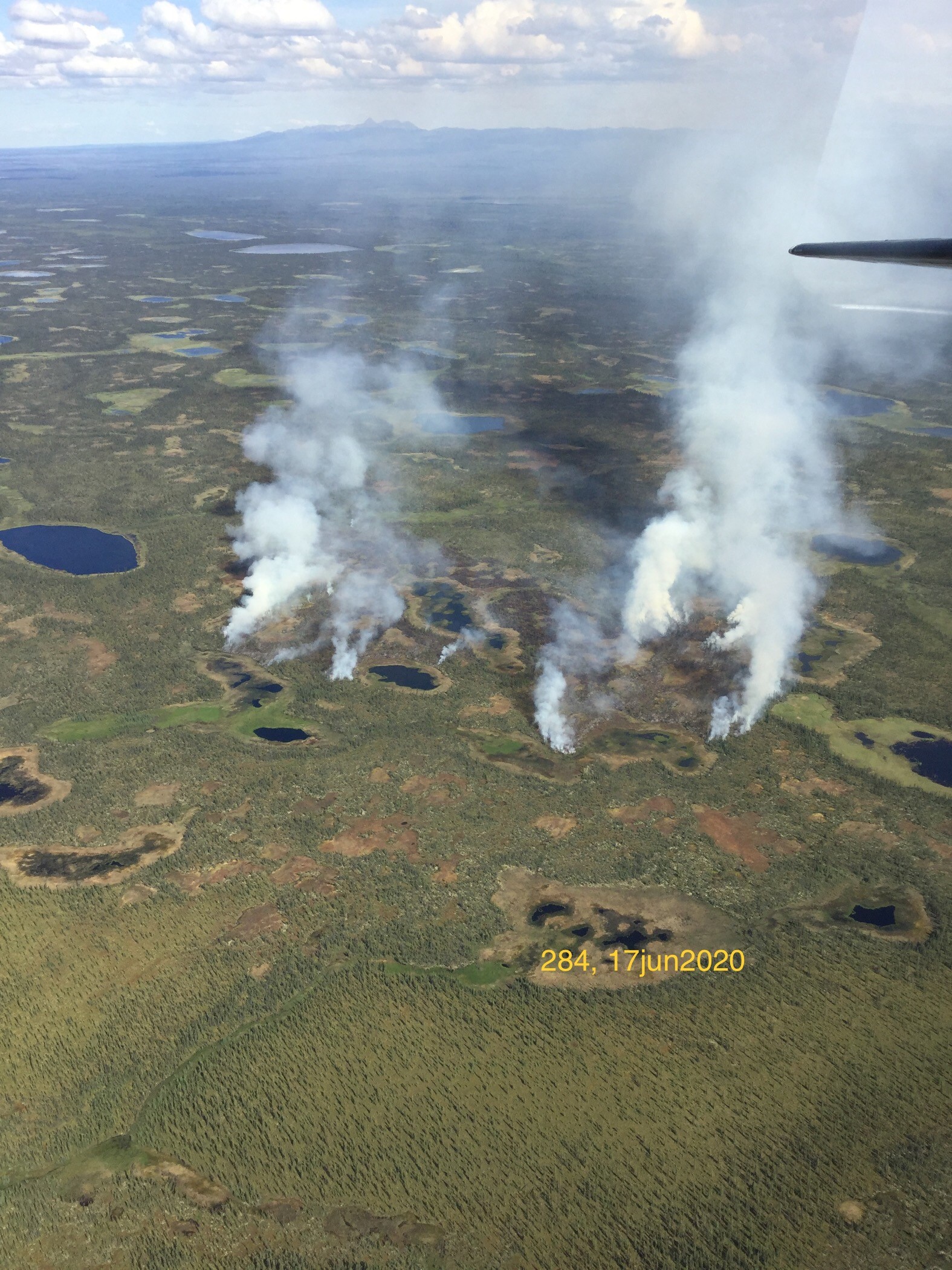 aerial view of smoke rising from a landscape dotted with ponds