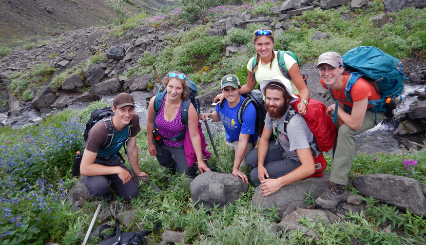 a group of students and researchers kneel next to a fossilized dinosaur track