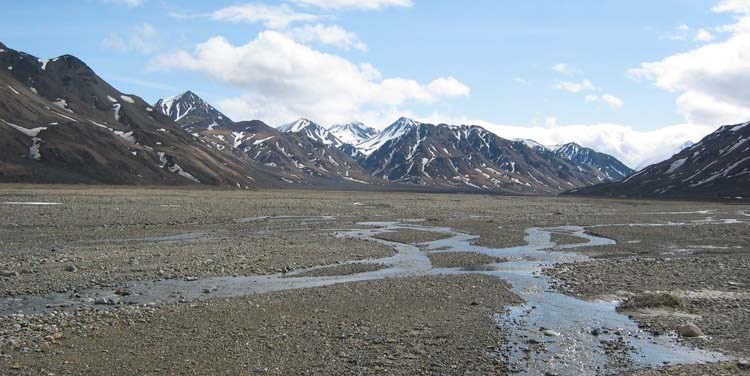 a wide, graveled plain leading up to brown, snow-dotted mountains