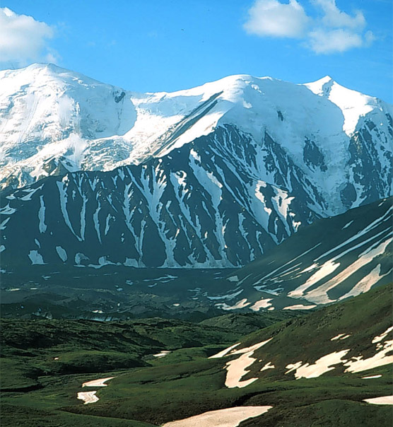 patches of snow on green hills, leading up to snowy mountains