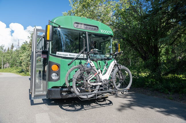 Two bikes on a bike rack mounted on the front of a green bus.