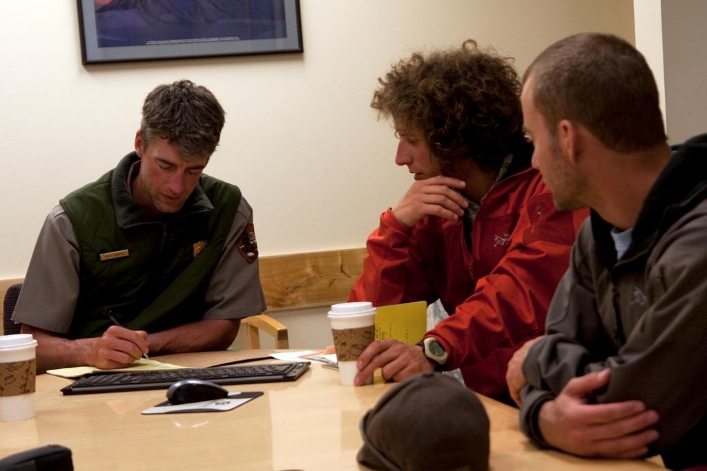 three men - two climbers and one ranger - sitting at a conference table three men - two climbers and one ranger - sitting at a conference table