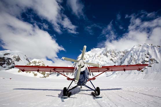 a small propeller plane sitting on a snowfield, with steep, snowy mountains in the background a small propeller plane sitting on a snowfield, with steep, snowy mountains in the background
