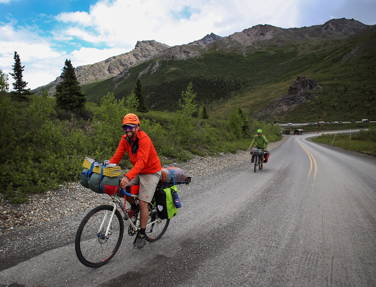 Two cyclists biking uphill on a road that changes from pavement to gravel