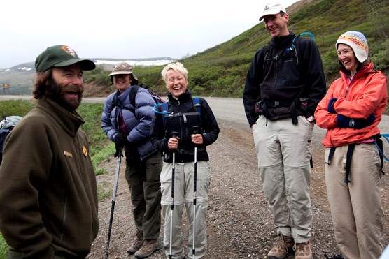 a male ranger and four hikers stand on a dirt road laughing