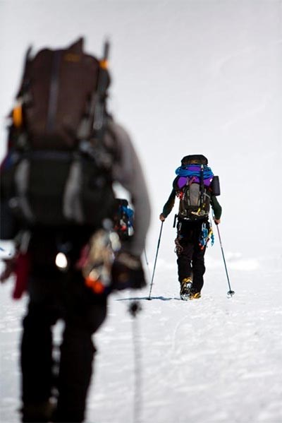 Two heavily-laden mountain climbers roped together, hiking on snow