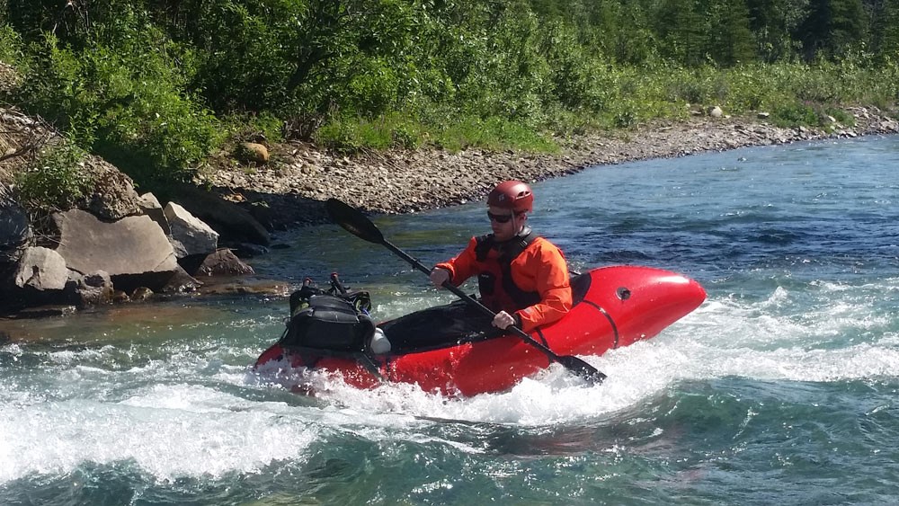 a man in a small red raft wearing a helmet and life jacket floats down a clear river